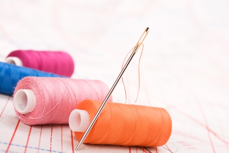Spool of thread and needle. Sew accessories on blurred background.