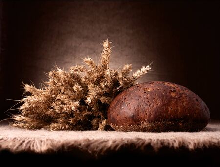 Loaf of bread and rye ears still life on rustic background