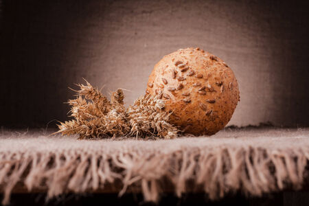 Loaf of bread and wheat ears still life on rustic background
