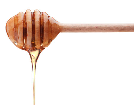 Honey dripping from a wooden honey dipper isolated の写真素材