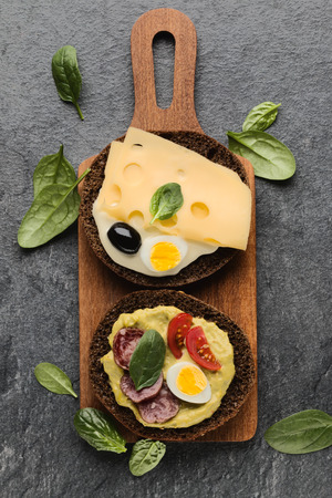 Open faced sausage sandwich canape or crostini on a wooden serving board  on dark stone background closeup. Top view.の写真素材