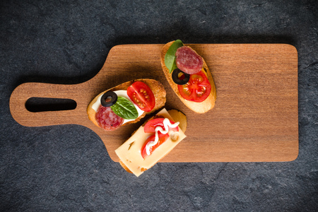 Open faced sandwich canape or crostini on a wooden serving board on dark stone  background closeup....