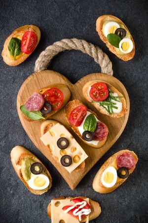 Open faced sandwich canape or crostini on a wooden serving board on dark stone  background closeup. Top view.の写真素材