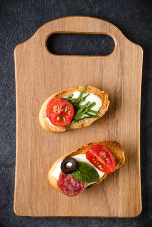 Open faced sandwich canape or crostini on a wooden serving board on dark stone  background closeup. Top view.の写真素材
