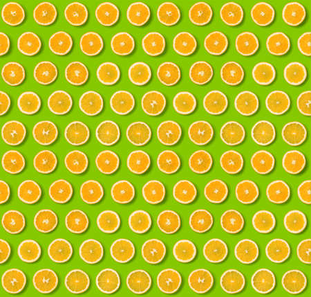 Seamless pattern of orange fruit slices on green background. Flat lay, top view. Food background. .  Pop art design, creative concept.の写真素材
