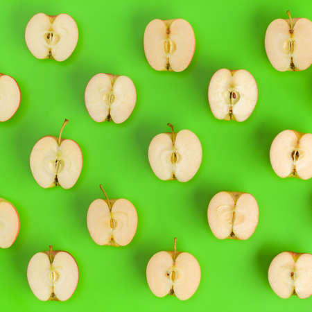 Fruit pattern on green background. Apple halves geometrical layout. Flat lay, top view. Food background..  Pop art design, creative summer concept.の写真素材