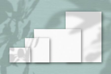 Several horizontal and vertical sheets of white textured paper against a grey wall background....