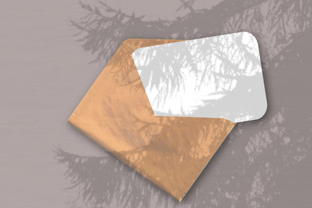An envelope with sheet of textured white paper on the brawn background. Mockup overlay with the...