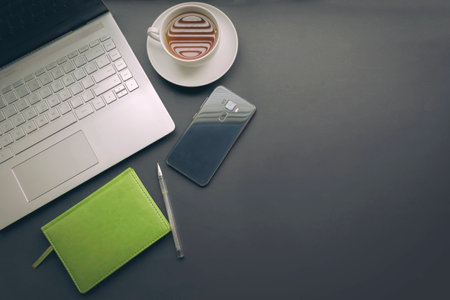 A set of tools for work. Laptop on a dark background, notepad for notes, phone. White mug with coffee. Top view, toned photoの写真素材