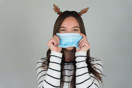 Beautiful young brunette with a medical protective mask on a gray background.の写真素材