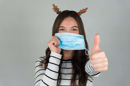 Beautiful young brunette with a medical protective mask on a gray background.の写真素材