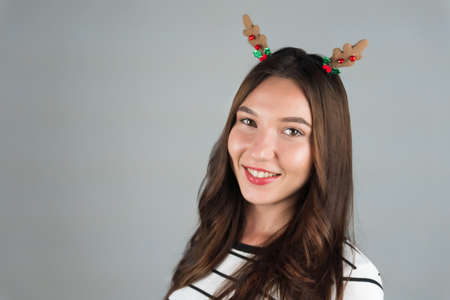 A happy young woman with Christmas decoration in her hair looks into the camera. Celebrating Christmas and New Year. High quality photoの写真素材