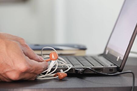 Hand hold earphone with white wire connect black laptop on computer tableの写真素材