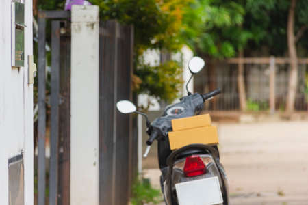 focus on cardboard box put on metal fence of house with asian delivery man wear hygienic mask and blue cap and holding phone background  at outside of houseの写真素材