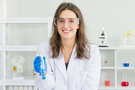 female scientist wear safety glasses and blue glove take chemicals into a test tube to study chemicals at laboratoryの写真素材
