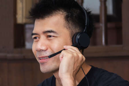 Asian man wear black T-shirt use black headphone  for work from home via conference call and looking...