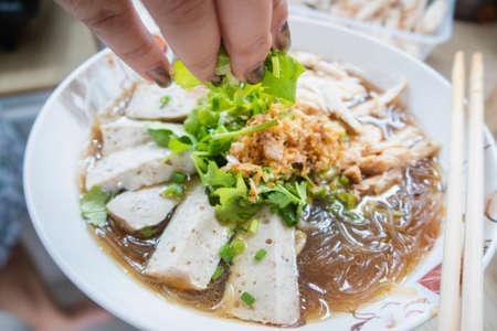 Boiled vermicelli with white pork sausage with vegetables; sprinkle in a bowl with chopsticks at kitchenの写真素材