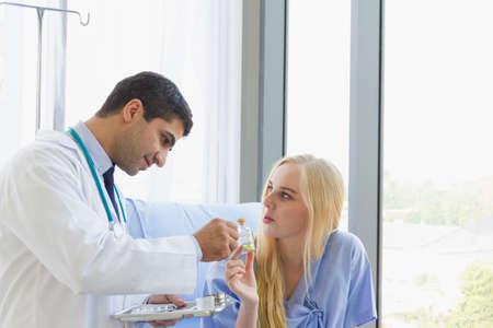 female patient holding a bottle of medicine asked a male doctor for directions on how to eat at hospital roomの写真素材