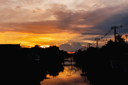 beautiful sunset with sky explode color with canal and small community via silhouette sceneの写真素材