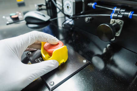 male hand wearing gloves presses an emergency button of an industrial machine for stop working