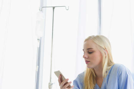 female patient holds the phone on the bed, the patient in the hospital room on day time