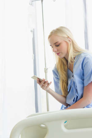 female patient holds the phone on the bed, the patient in the hospital room on day timeの写真素材