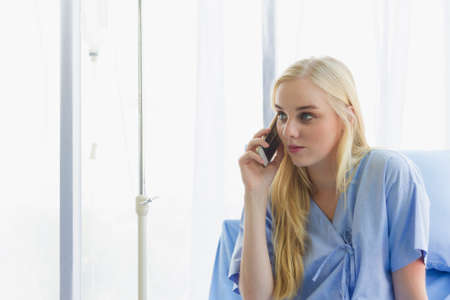 female patient holds the phone on the bed, the patient in the hospital room on day timeの写真素材