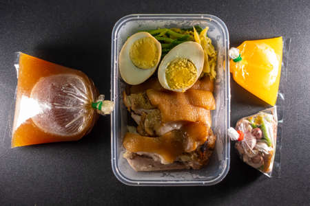 Stewed pork leg in a plastic box with sauce, broth, paprika, garlic, placed on a black table with lightsの写真素材