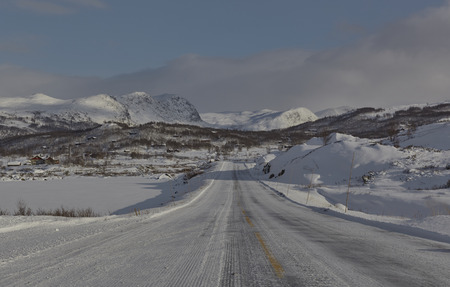 Road 53, almost entirely covered in snow, in Sogn og Fjordane province of Norway, on a bright sunny day in November. The road is leading to mountains visible in the distance.の写真素材