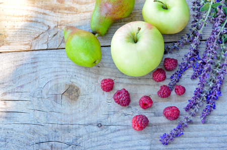 apples and pears and raspberries with a field of purple flowers on a wooden Boardの写真素材