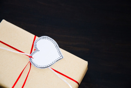 gift wrapped in kraft paper with a label heart drawn on a black wooden backgroundの写真素材