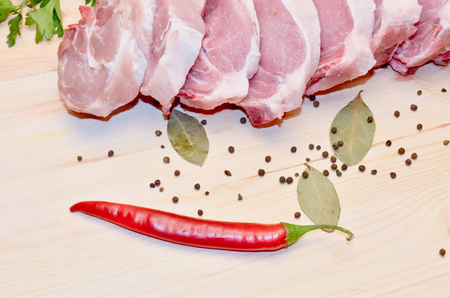 Pieces of pork meat on wooden background next to red pepper and pepper and Bay leaf. Selective focus.の写真素材