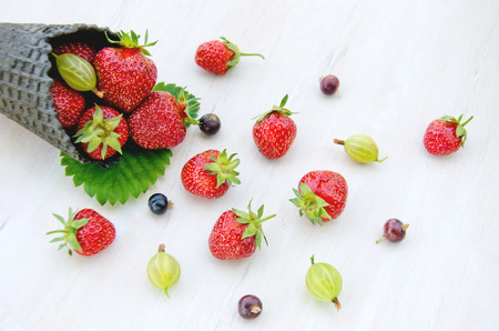 green and black cone ice cream filled with strawberries and gooseberry and black currant it fell out of the horn, lies on a wooden light background and strawberry leaves close upの写真素材