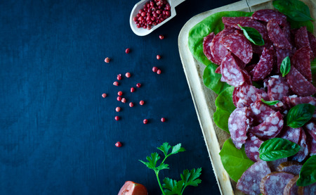 sliced salami pile on wooden Board with tomatoes and Basil leaves with salad on a wooden black background selective focusの写真素材