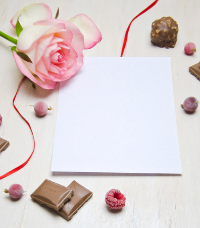 template paper for writing near rose chocolate and berry pieces and ribbon on white wooden background selective focusの写真素材
