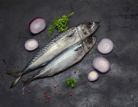 sea fish raw mackerel and onion and spices on a black table selective focus