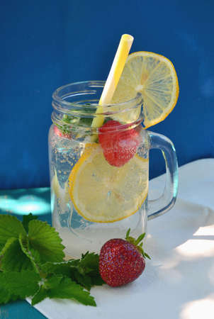 Natural lemonade in a jar with mint leaves and lemon and strawberries on a blue background. A cooling natural drink.Selective focus.の写真素材