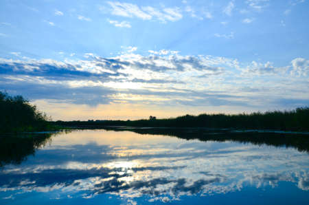 river in the morning sunrise clouds are reflected in the water reeds on the edges of the river...
