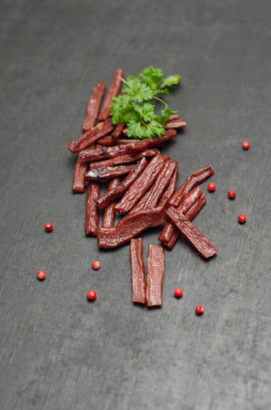 Dried sausage with parsley and red pepper on a black background
