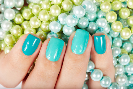 Nails with manicure covered with nail polish on colored pearls backgroundの写真素材