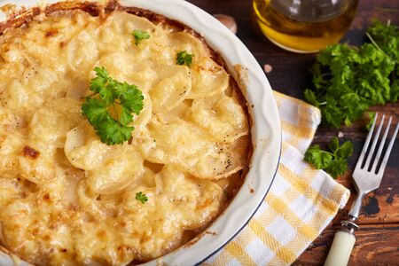 Potato gratin. Slices of potato backed with cream sauce, garlic and cheese, decorated with parsley leafs. Rustic style. Vegetarian dish.の写真素材