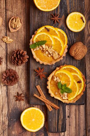 Mini tart pies with orange, custard cream and walnuts on wooden background. Sweet Christmas dessert.の写真素材