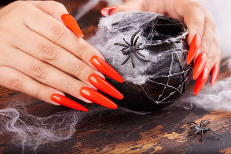 Hands with long artificial manicured nails colored with orange nail polish and Halloween decorationsの写真素材