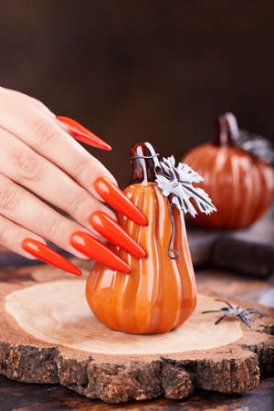 Hand with long artificial manicured nails colored with orange nail polish and pumpkin Halloween decorationsの写真素材
