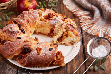 Yeast dough wreath pie with apples, cinnamon and raisins covered with sugar powder. Braided ring shaped cake.の写真素材