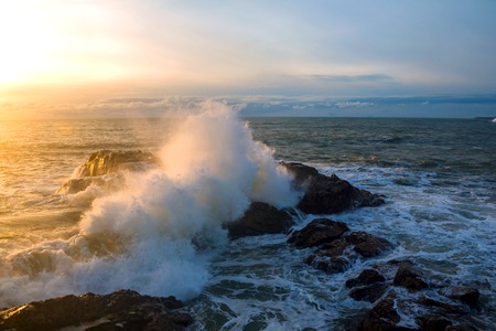 Waves of the Atlantic Ocean crashing against a rock at sunset.の写真素材