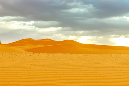 Beautiful sand dunes at sunrise in the Sahara Desert. The sun's rays make their way through the clouds, Moroccoの写真素材