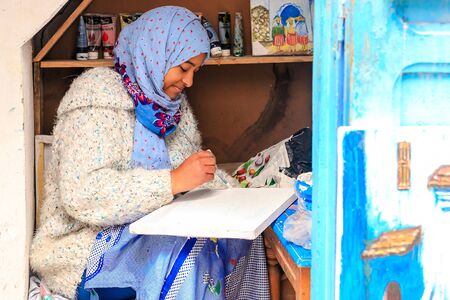 A beautiful Moroccan girl, a Muslim, street artist paints a picture with a brush in a small workshop. Chefchaouen, Morocco, Africaのeditorial素材
