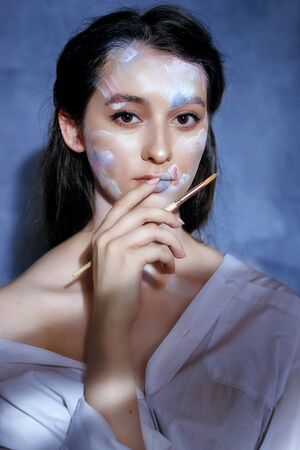 Creative fashion beauty portrait of a beautiful young woman with an artistic tassel in her hands. Model girl with professional make-up and body art on gray background.の写真素材