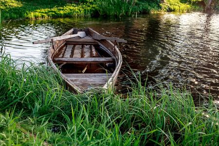 A small wooden rowing boat with a broken bottom on a calm lake near the shore. Belarusの写真素材